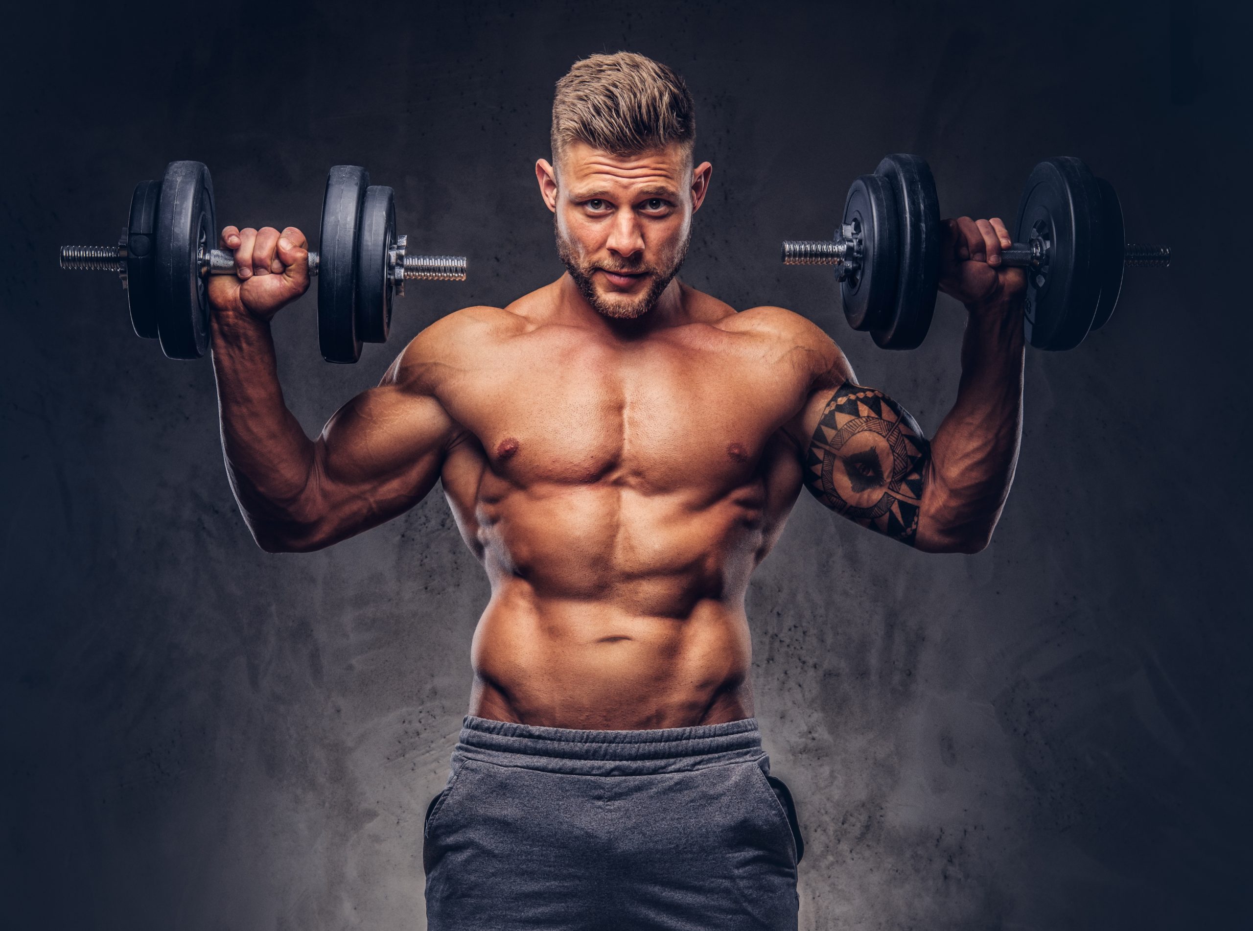 Handsome shirtless tattooed bodybuilder wearing sports shorts, posing in a studio. bodybuilder